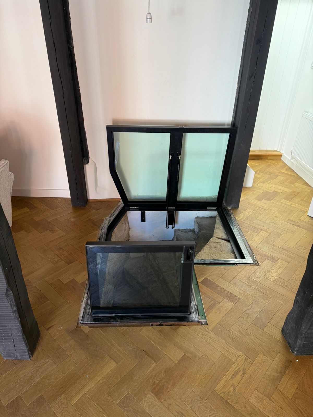 Hinged glass floor doors in open position showing powder coated black steel frame, L-shaped opening, Burwash